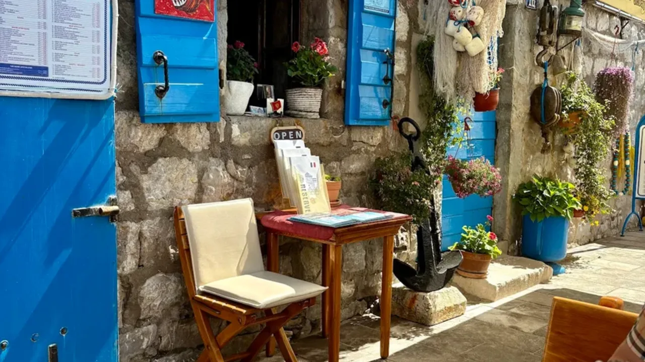 Stone facade of a traditional konoba with blue shutters, fishing nets and flowers on the Montenegrin coast