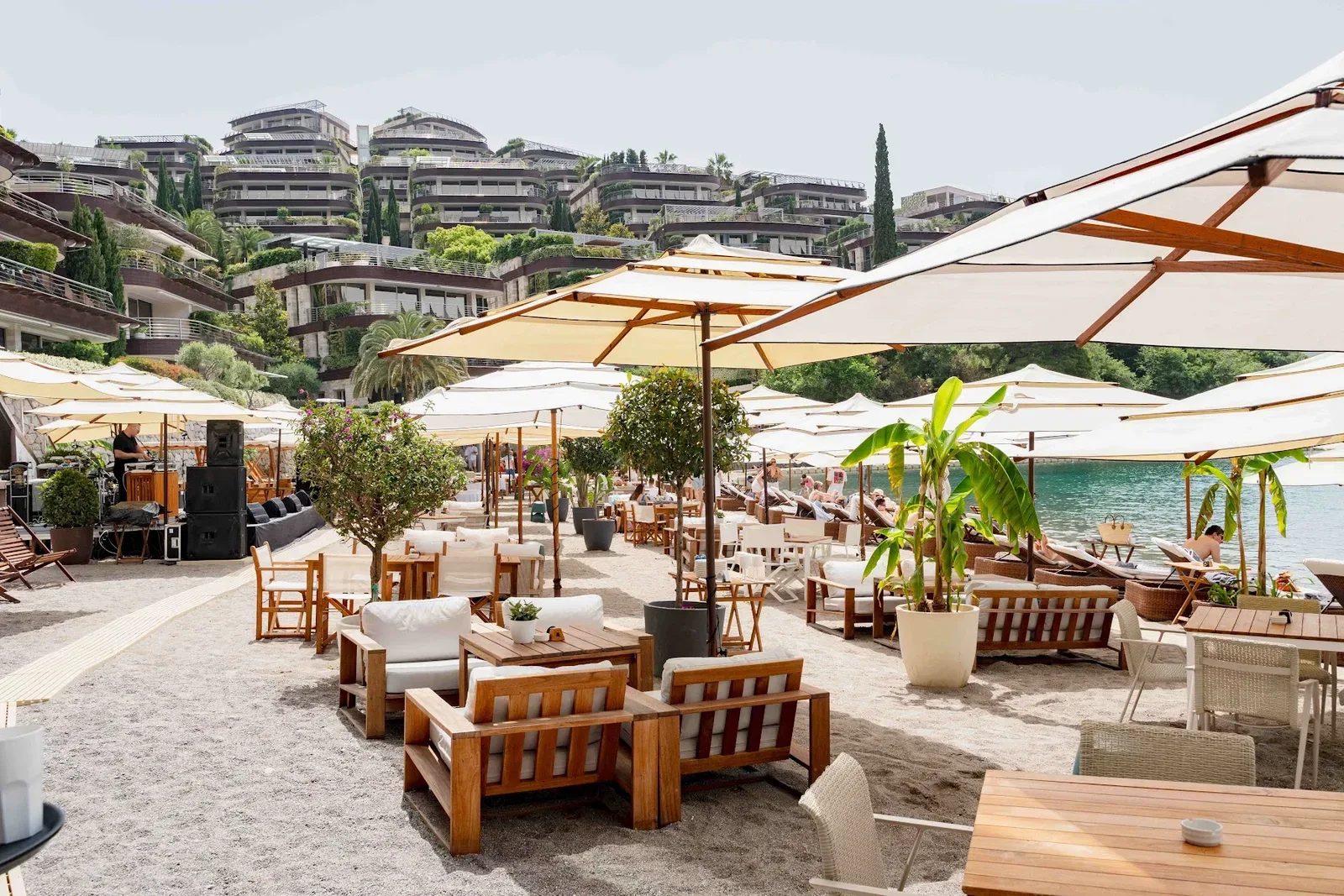 Cream parasols, teak sofas and daybeds on the sand at Dukley Beach & Bar, with the terraced Dukley Gardens buildings on the hillside behind