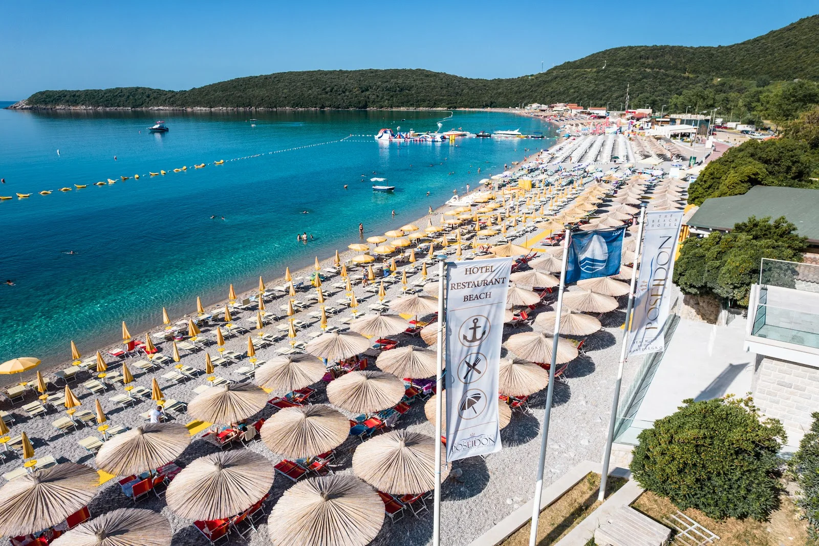 Aerial view of Hotel Poseidon's beach with thatched umbrellas and turquoise water
