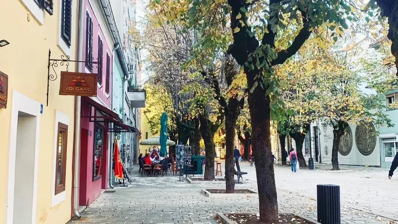 A tree-lined pedestrian street in Cetinje's old town, lined with cafés and pastel townhouses under autumn foliage