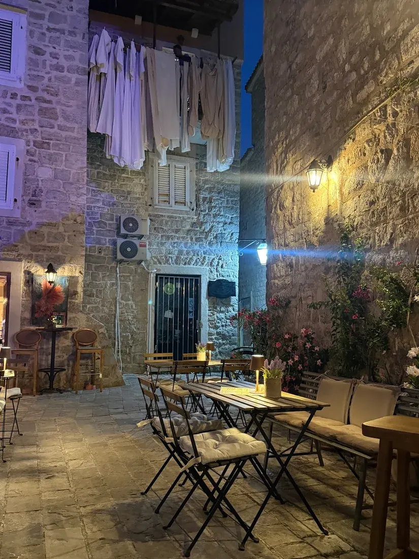 Candle-lit bistro tables in a stone courtyard against the Old Town walls at Freedom Bar & Prosciutteria in Budva at night