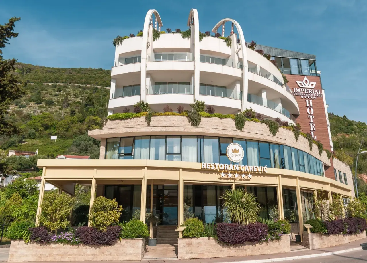 The curved white facade of Hotel Imperial Conference & Spa above its garden restaurant near Budva