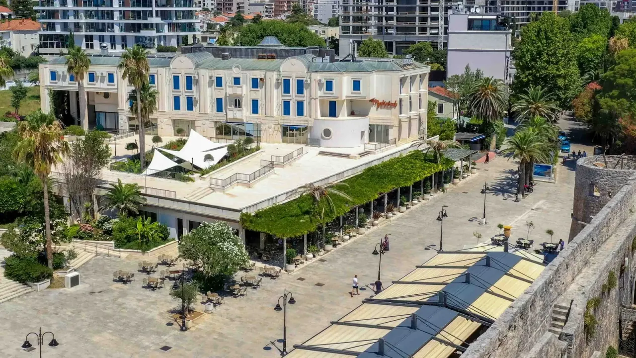 The white Hotel Mogren building above its vine-shaded promenade terrace beside Budva's old town
