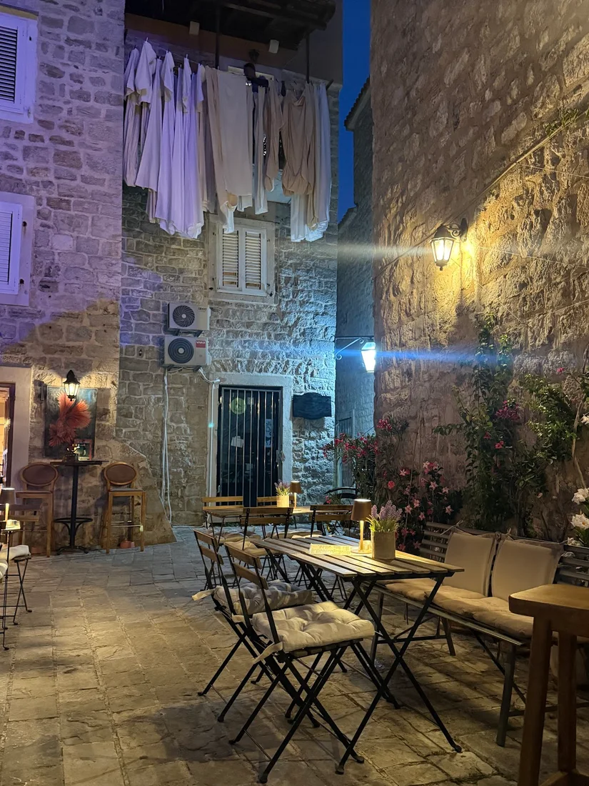 Candle-lit bistro tables in a stone courtyard against the Old Town walls at Freedom Bar & Prosciutteria in Budva at night