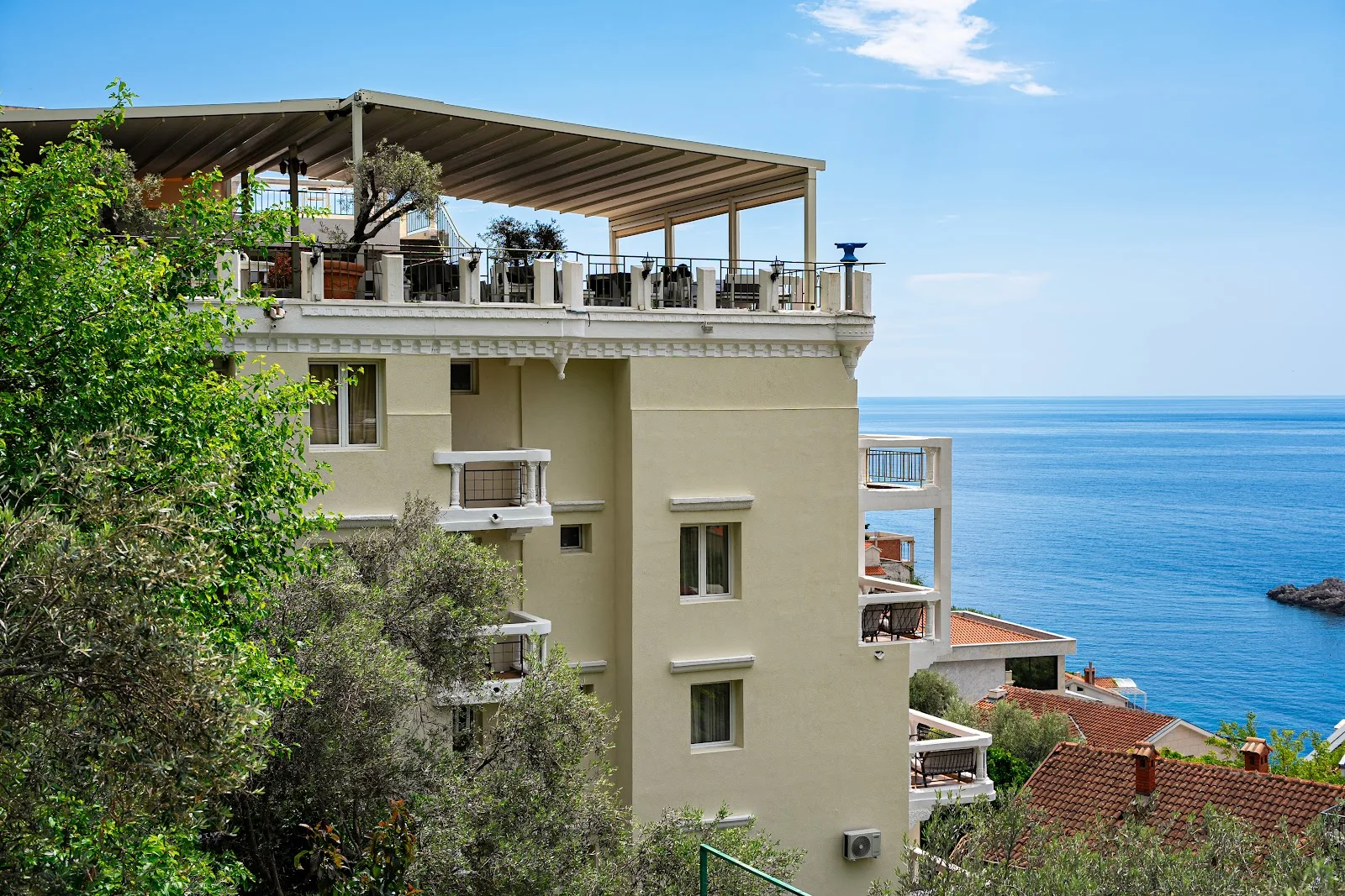 The cream facade and rooftop terrace of Hotel Adrović above the sea at Sveti Stefan