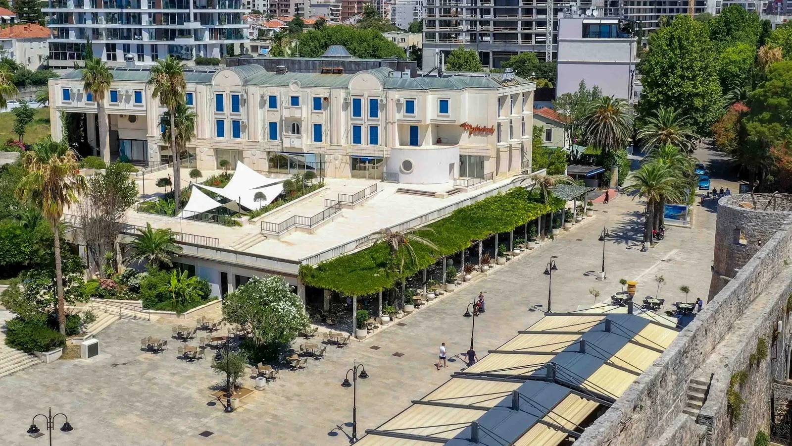 The white Hotel Mogren building above its vine-shaded promenade terrace beside Budva's old town