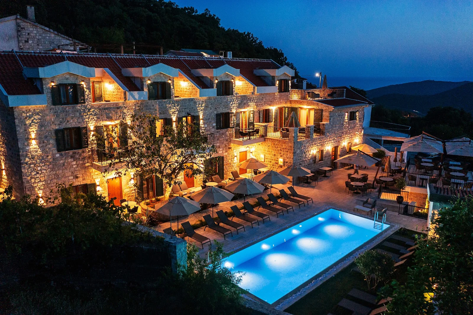 Stone-built Hotel Ruzmarin lit up at dusk above its pool and terrace in the hills above Budva