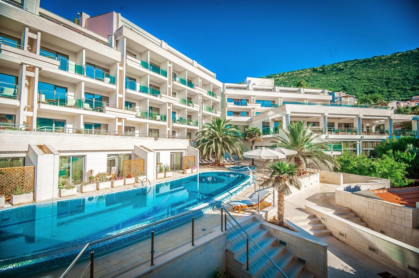 The large outdoor pool and terraces of the MonteCasa Spa & Wellness Hotel against the hills at Petrovac