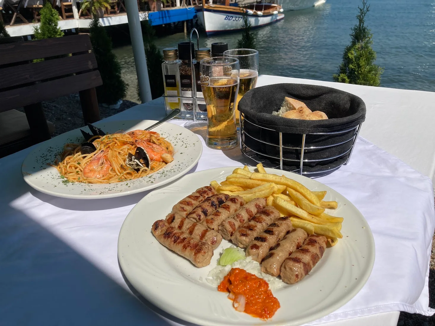 Seafood pasta and grilled ćevapi on a waterfront table overlooking fishing boats at Restaurant Jadran on the Budva marina