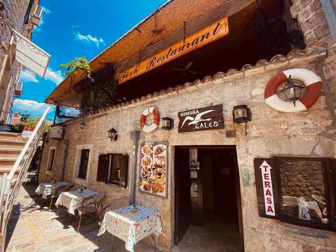 Stone façade hung with life rings and a fishing net under the Fish Restaurant and Konoba Galeb signs in Budva's Old Town