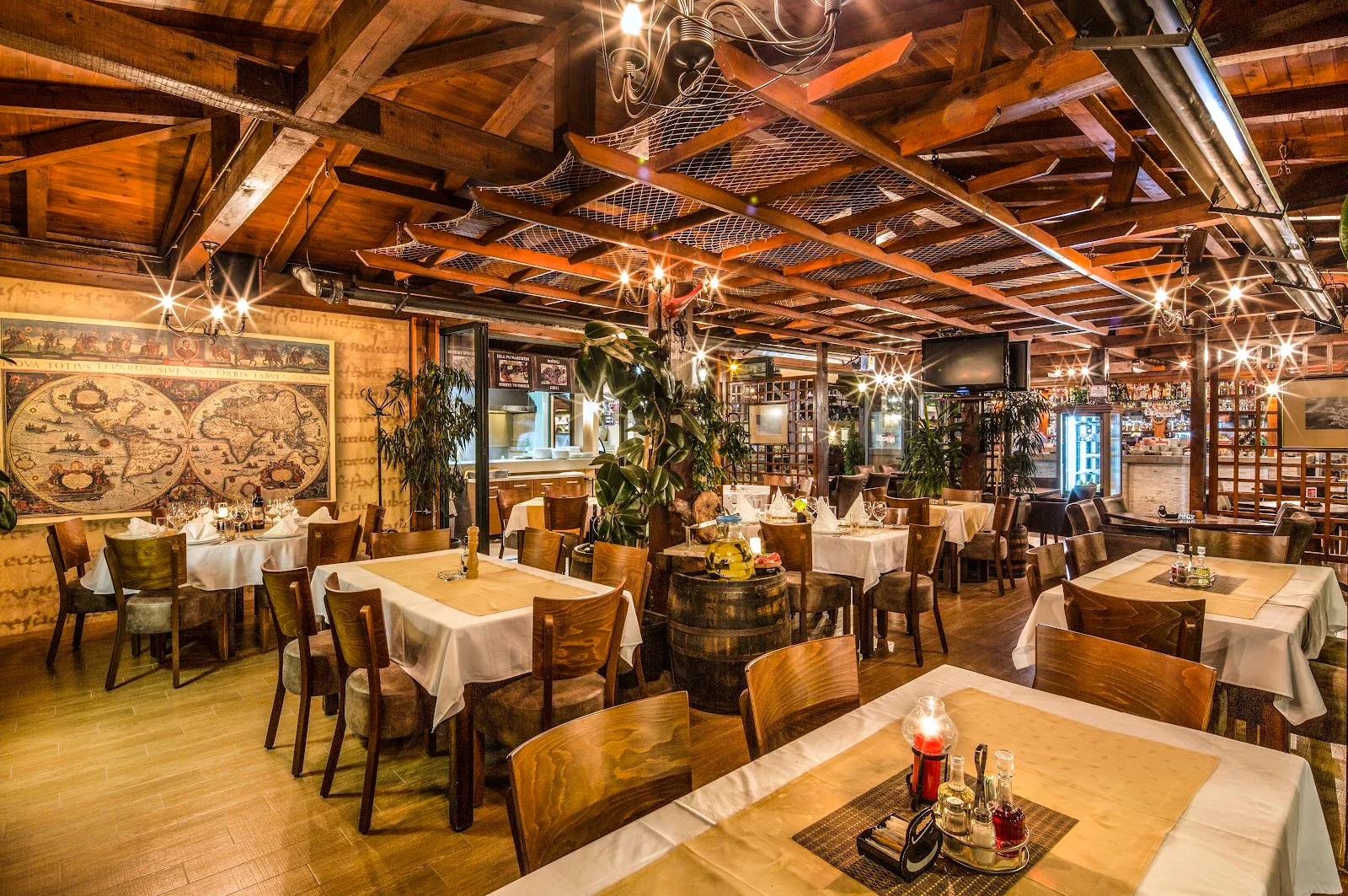 Warm timber-beamed dining room hung with fishing nets and an antique world map at Zeleni Gaj in Budva