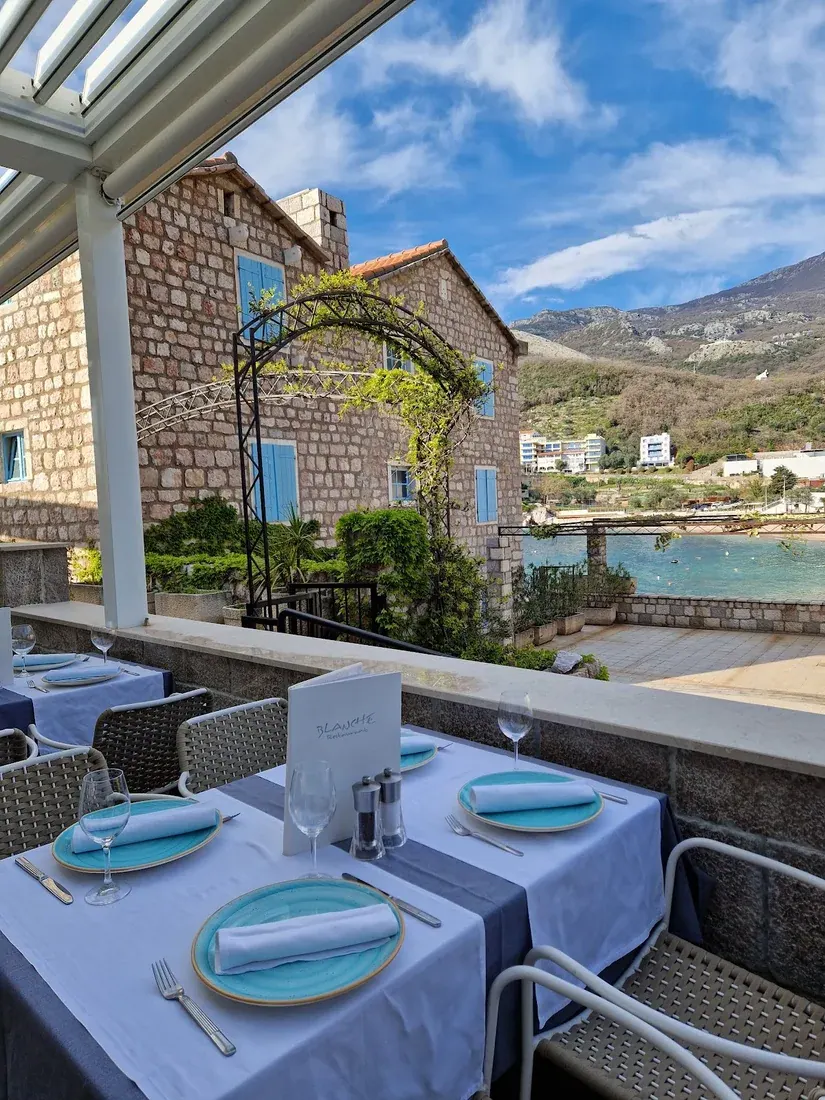 White-linen tables under a glass canopy looking over the Pržno beach and bay at Blanche