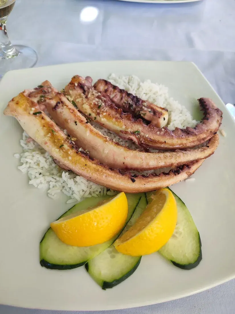A plate of grilled octopus tentacles over rice with lemon and cucumber at Konoba Bonaca in Petrovac