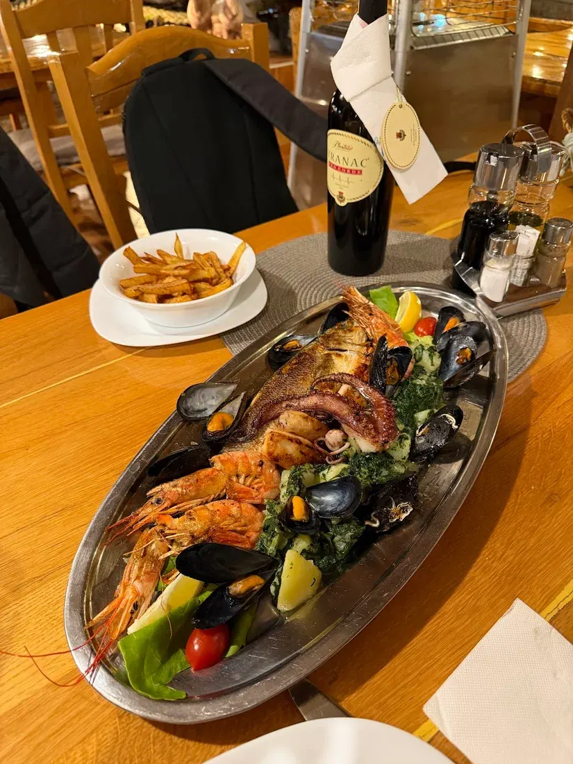 A mixed seafood platter of grilled fish, prawns and mussels with a bottle of Vranac wine on a wooden table at Lim Restaurant in Budva